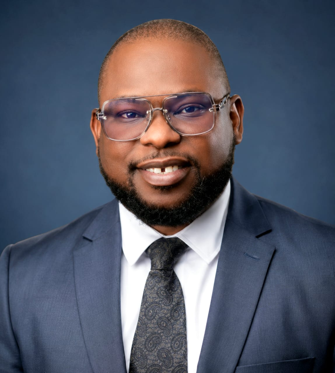 Portrait of a Nigerian real estate professional in a navy suit, white shirt and patterned tie.