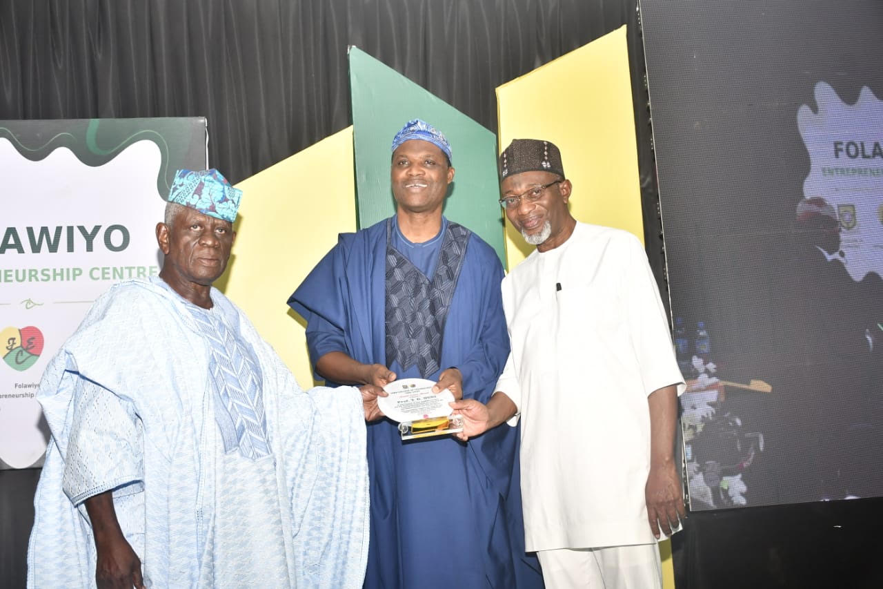 Three men pose on stage at the Folawiyo Entrepreneurship Centre lecture, with one receiving an award.